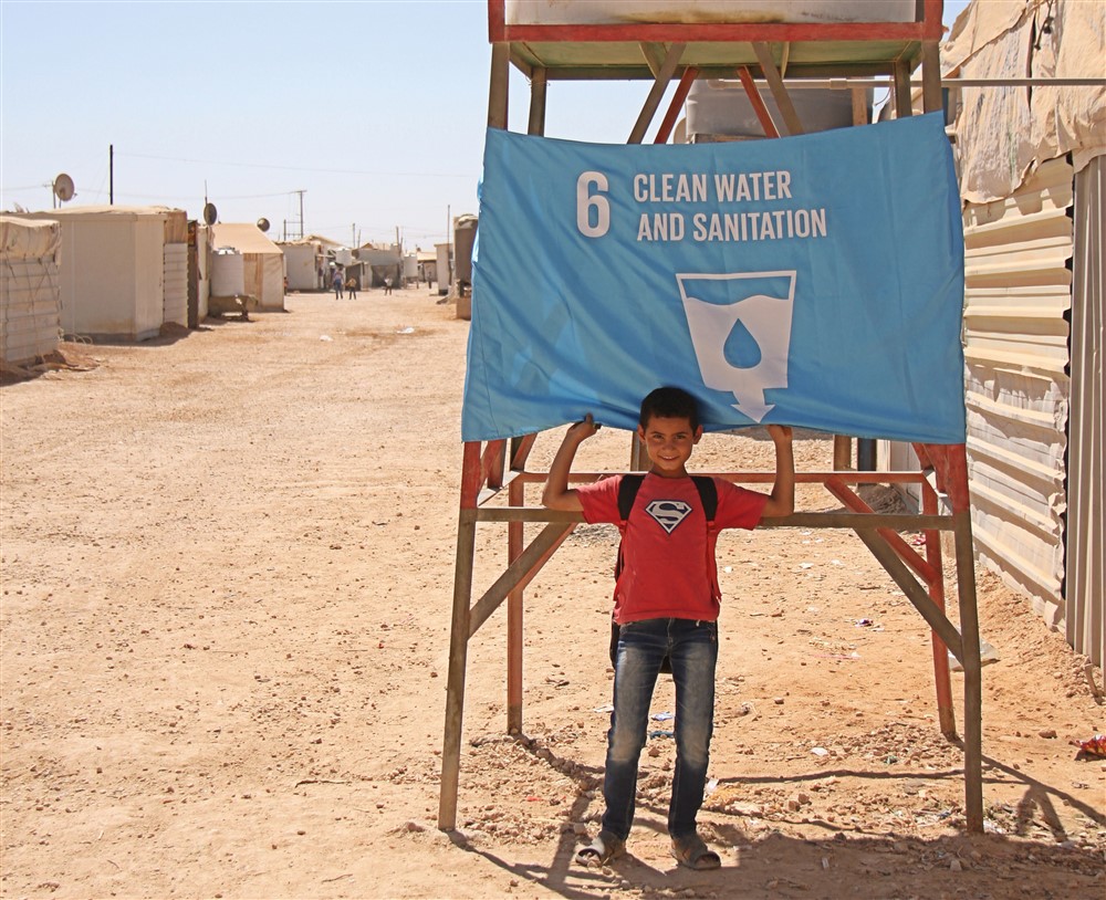 A child from the Za’atari Refugee Camp in Jordan raised a flag to represent Goal 6, Safe Water and Sanitation. Photo: UNICEF Jordan/badran